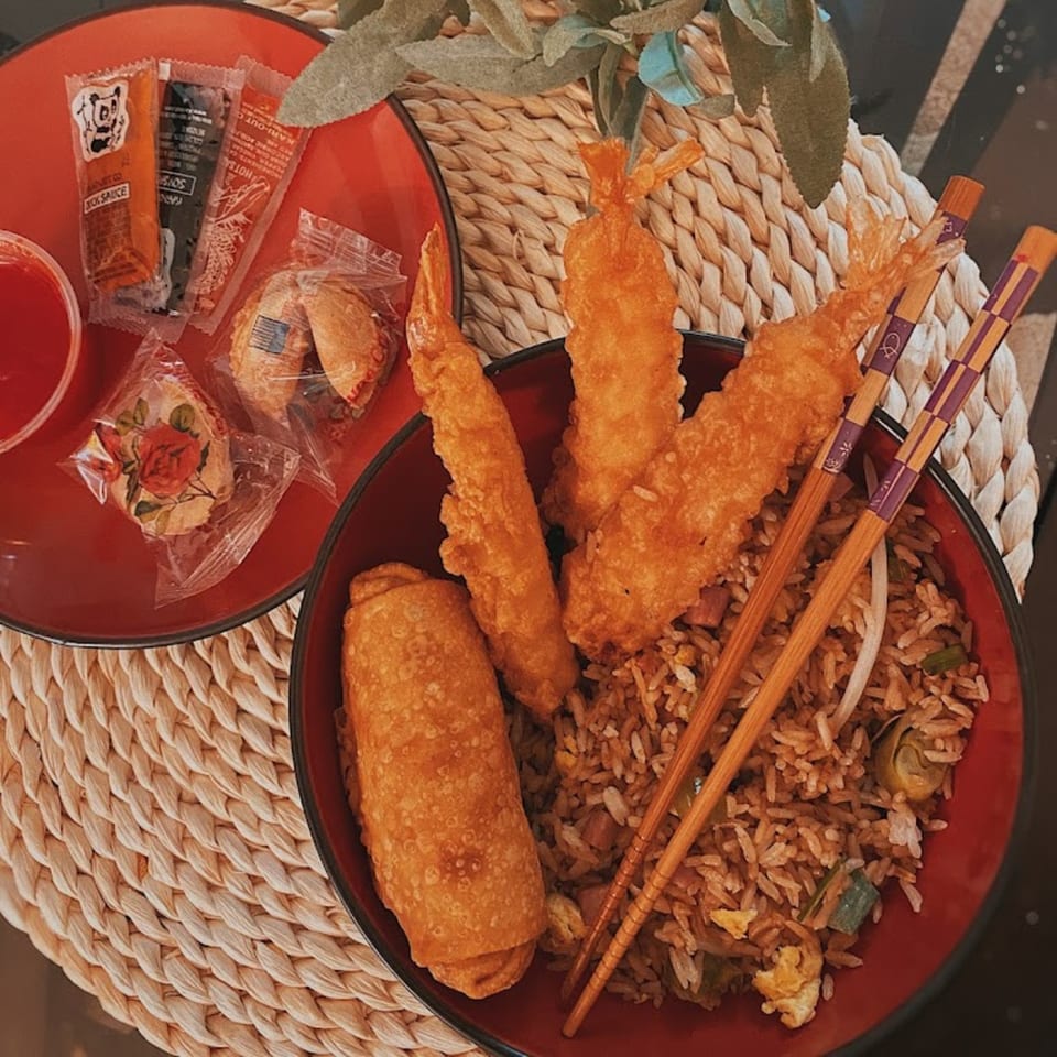 Chinese fried rice with egg roll, fried shrimp, sauces, and fortune cookies on a woven mat.