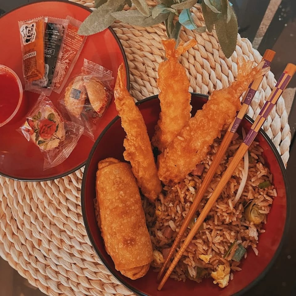Chinese meal with fried rice, egg roll, shrimp tempura, sauces, and fortune cookies on a woven mat.