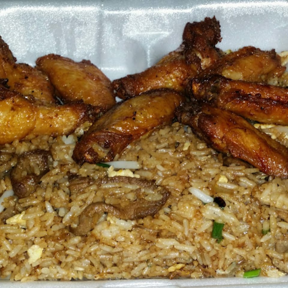 Golden-brown fried chicken wings arranged over a bed of savory fried rice in a white takeout container.