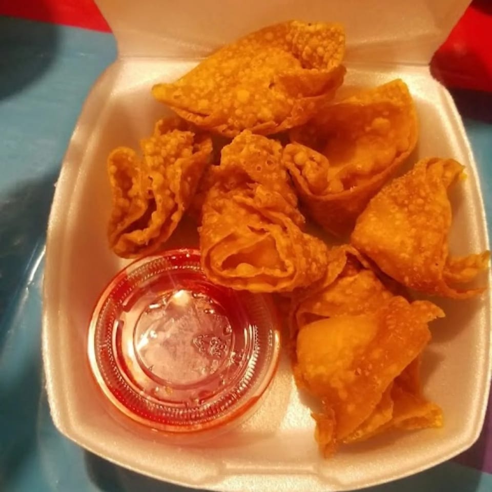 Golden-fried crab rangoon and sweet and sour sauce in a white takeout container.