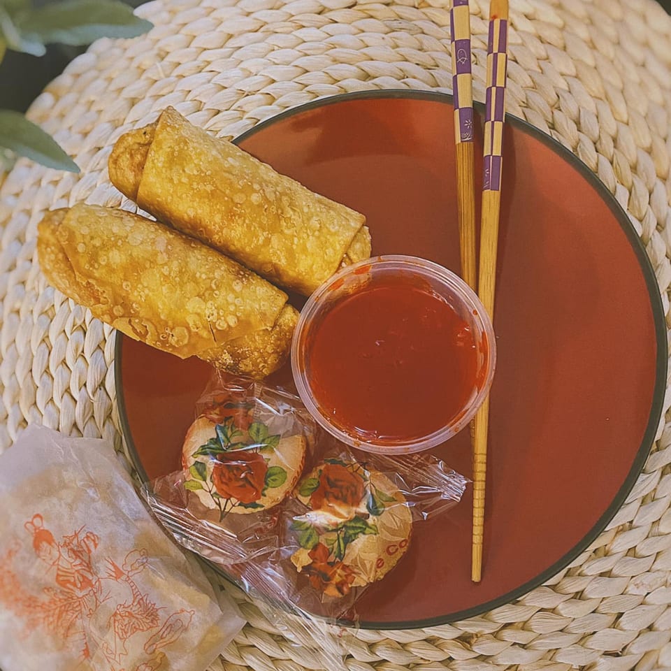 Two golden egg rolls, red dipping sauce, fortune cookies, and chopsticks on a red plate.